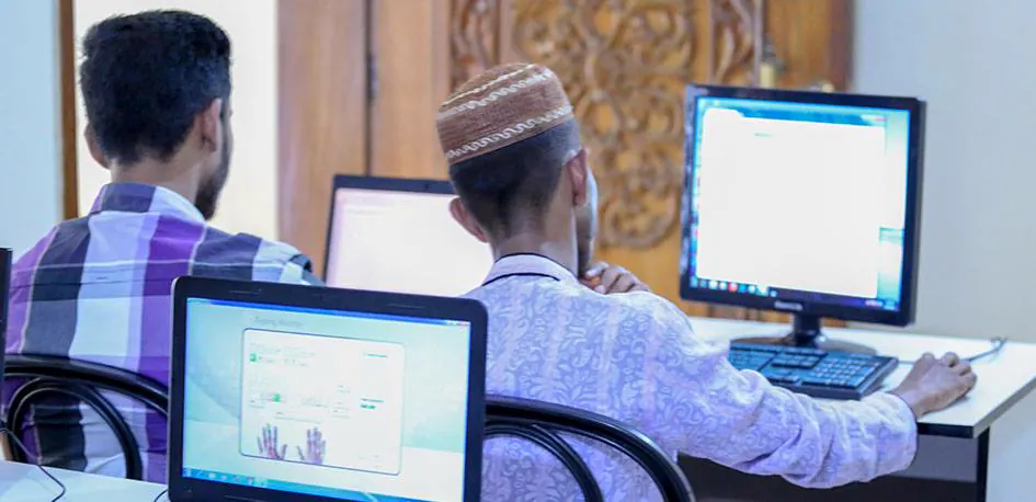 A student in an embroidered cap working at a monitor